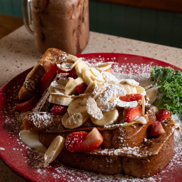 French toast topped with strawberries, bananas, powdered sugar, and a side of kale.