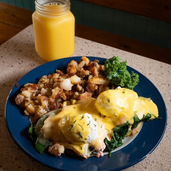 Eggs Benedict with hollandaise sauce, home fries, and kale, served with orange juice.