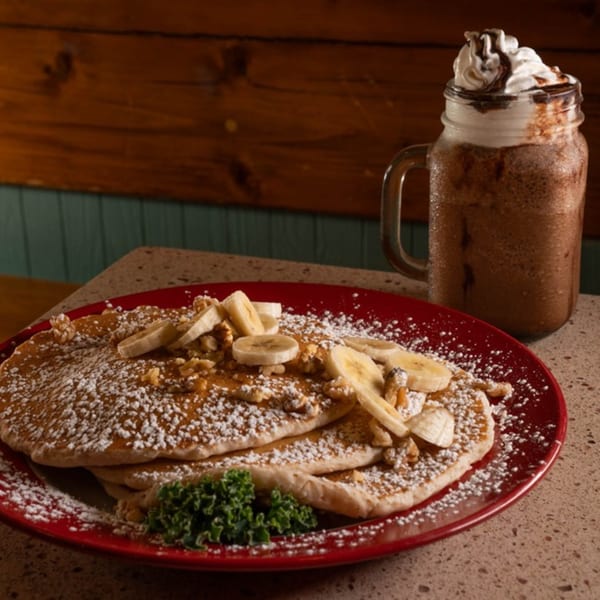 Pancakes with bananas, walnuts, powdered sugar, and a chocolate milkshake with whipped cream.